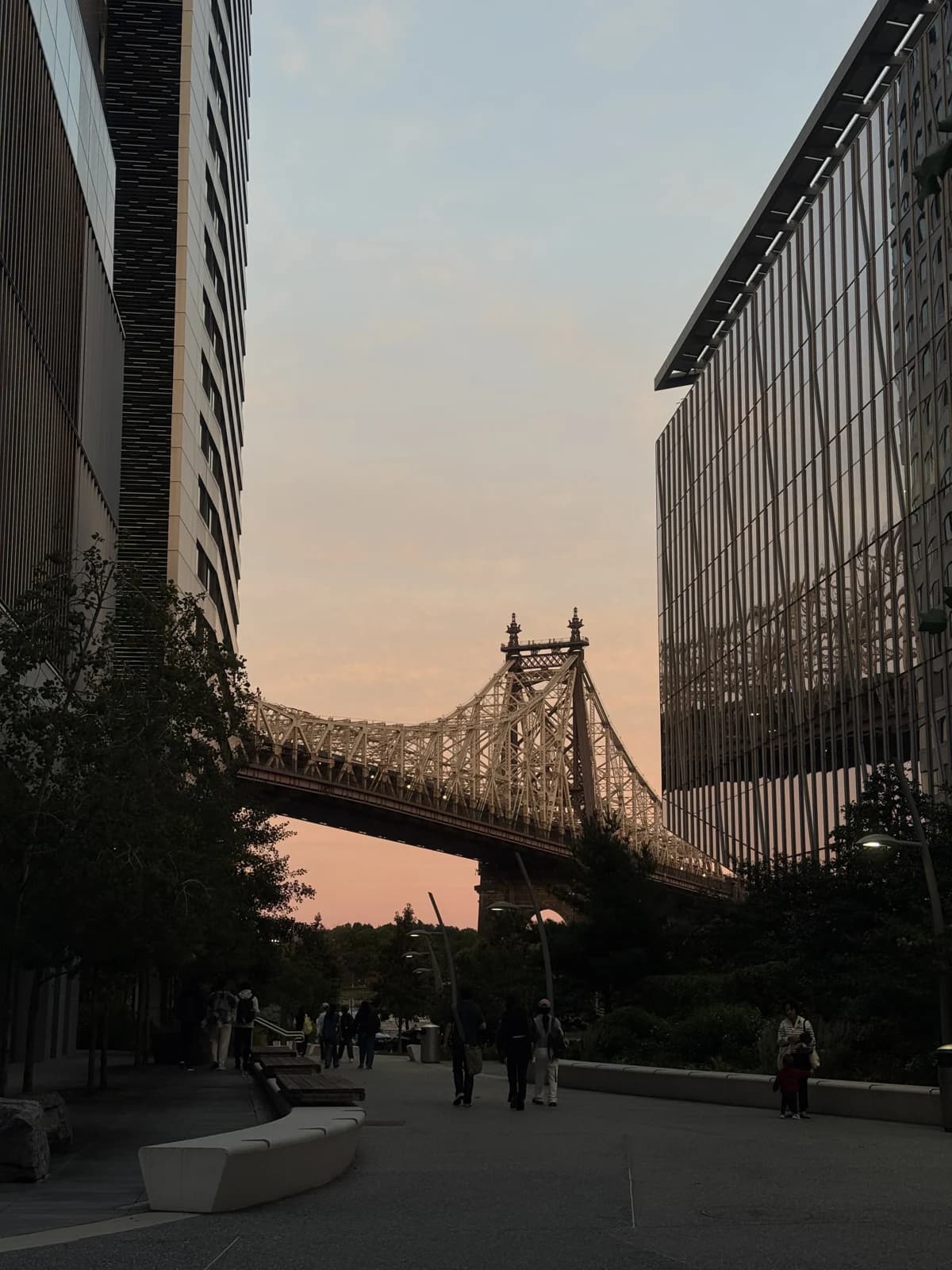 A bridge between modern buildings beneath a peach sunset sky