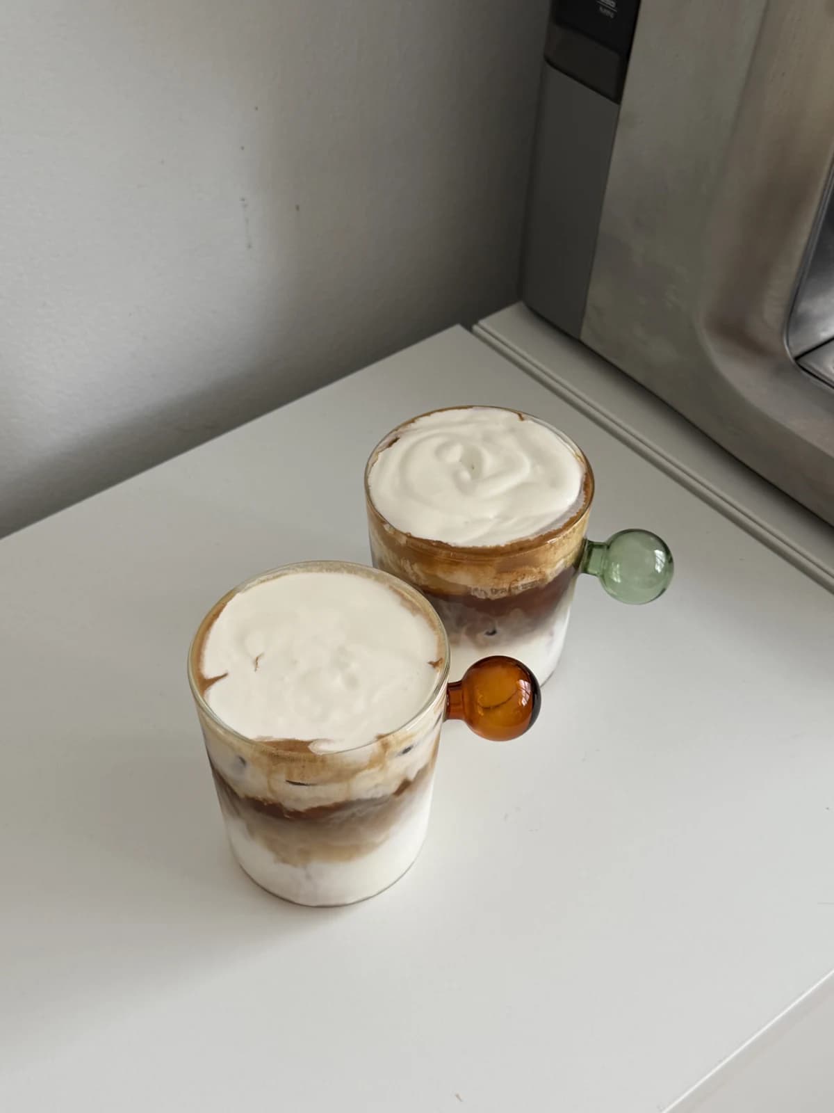 Two iced coffees in glasses with amber and green handles